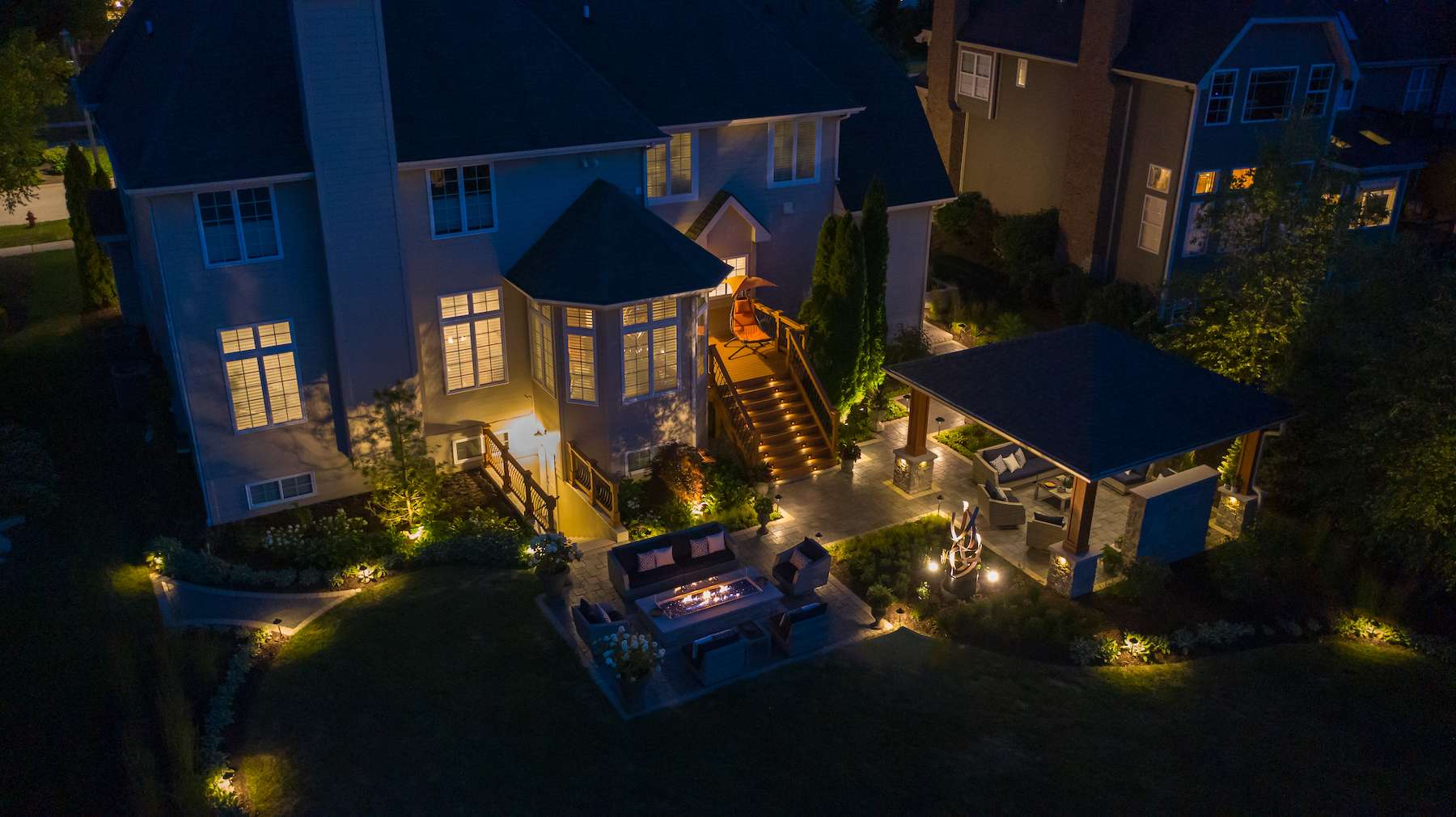 aerial photo of outdoor living space in backyard with fire table and pavilion at night
