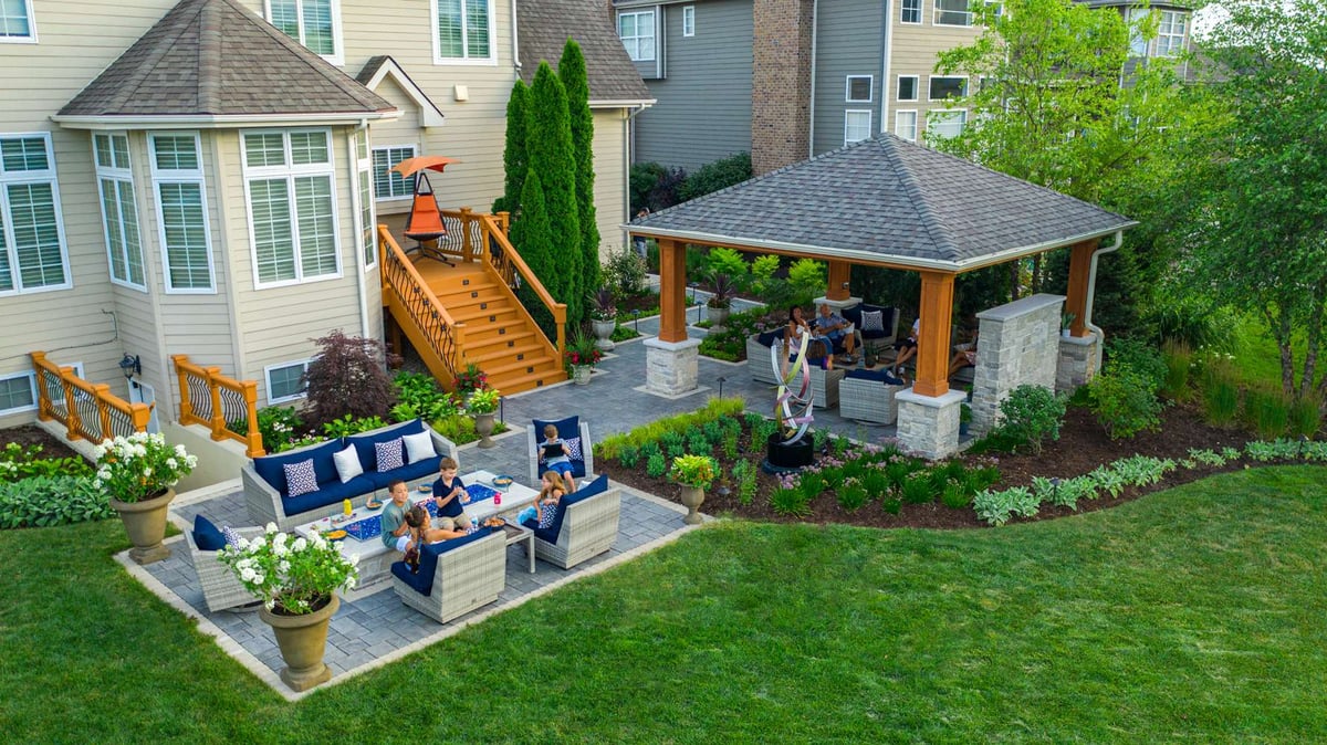 family sits in backyard near fire table and under pavilion