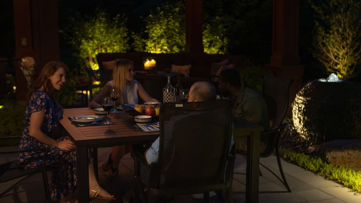 friends eat at patio table outside with landscape lighting