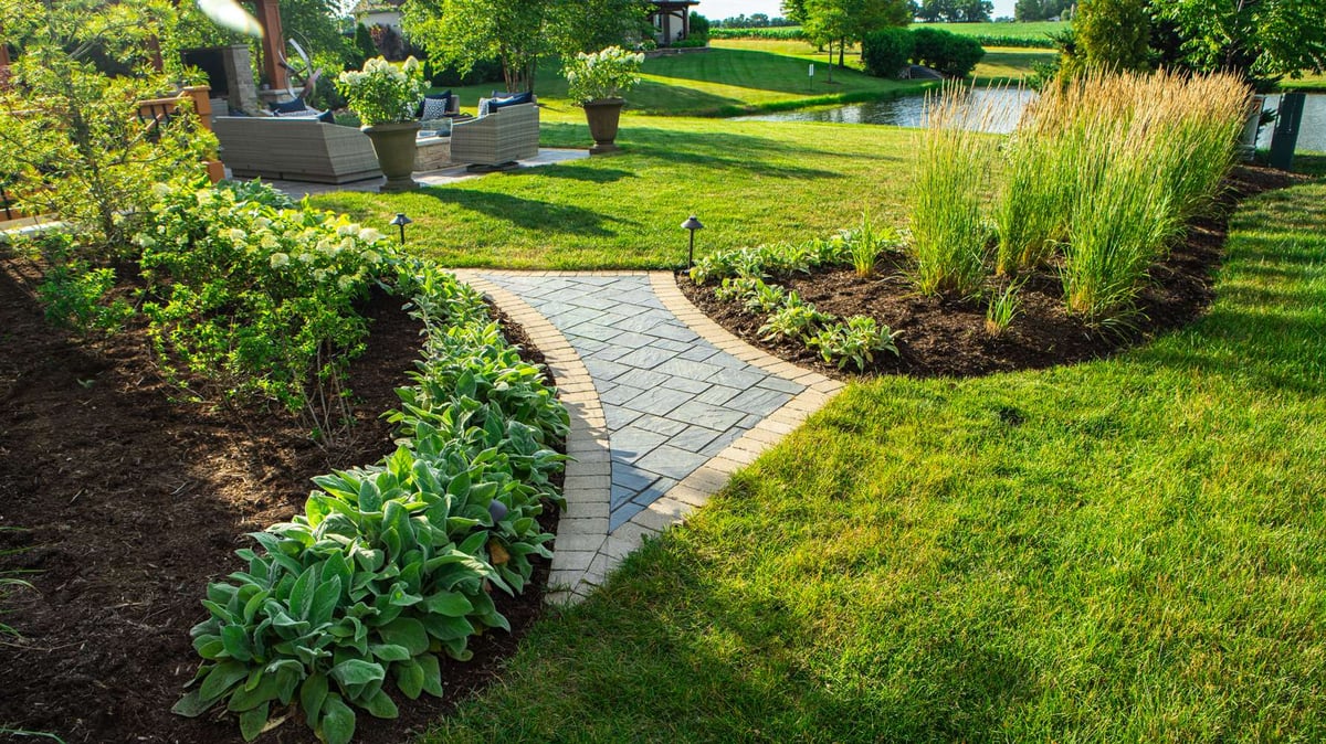 healthy plantings and grass with pathway to backyard outdoor entertaining area