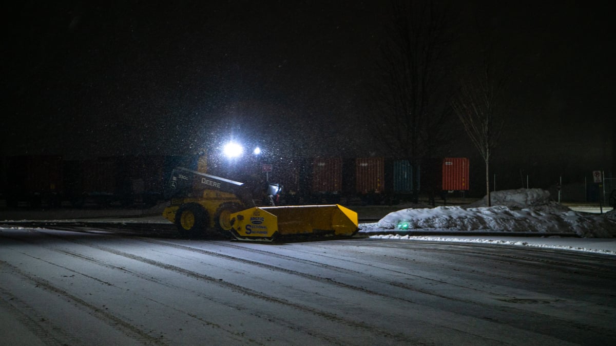 skid loader moves snow at night on commercial property
