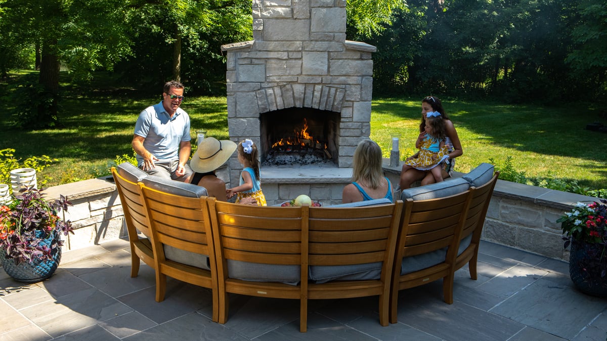 family sits around large outdoor fireplace